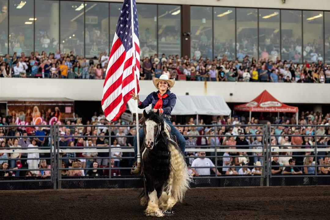 A rider carrying the American flag in front of a packed grandstand